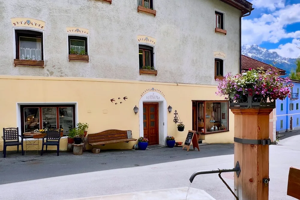 Die Fassade der Familielodge La Randulina am Dorfplatz, mit dem Brunnen davor.