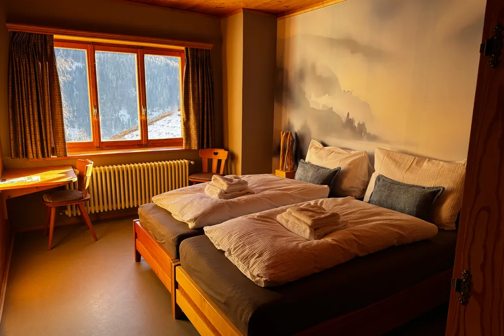 Ein Zimmer mit zwei Betten, Handtüchern auf der Bettdecke und einem Wandbild mit Bergen.