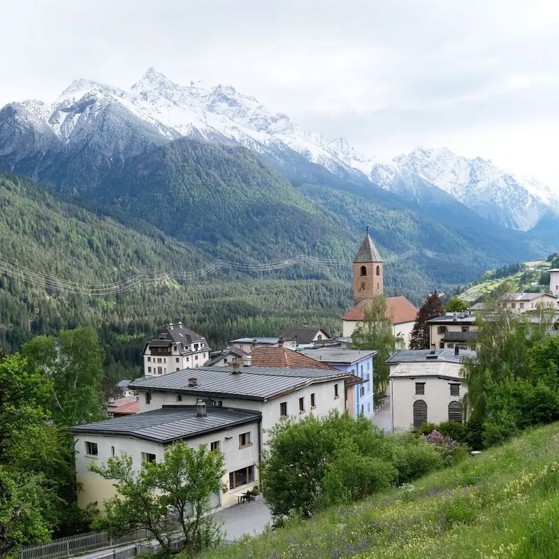 A mountain village in summer, with the church tower and the snowy mountains behind.