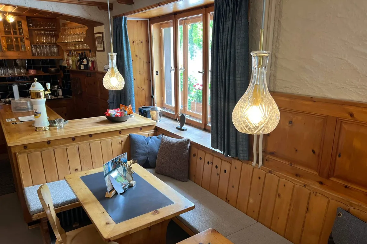 De gezellige houten Stube van de lodge, met glazen hanglampen, een hoekbank en een tafel bij het raam.