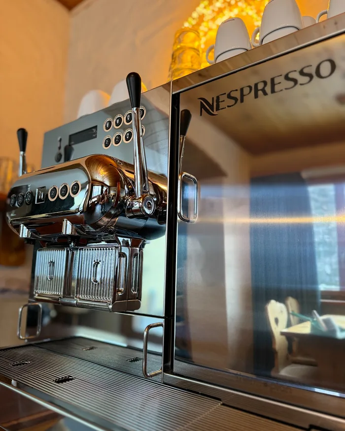 Een glanzende Nespresso-koffiemachine van chroom, met witte kopjes erop gestapeld en warm licht op de achtergrond.