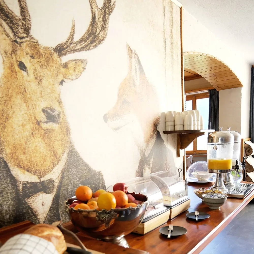 Het ontbijtbuffet van de lodge voor een groot wandschilderij van een hert en een vos, met een schaal fruit en sap.