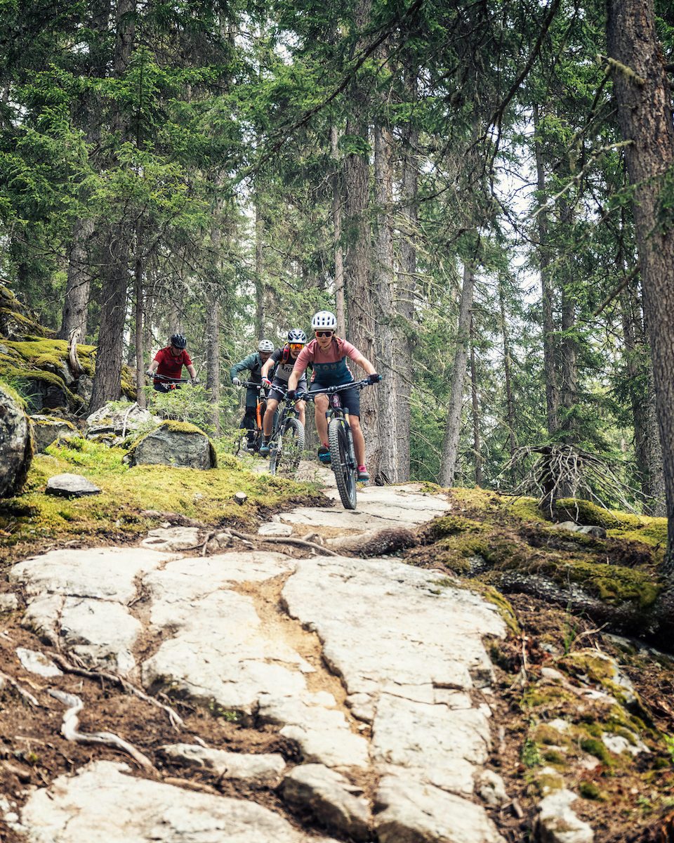 Mountainbikers rijden over een rotsachtig pad door het bos.