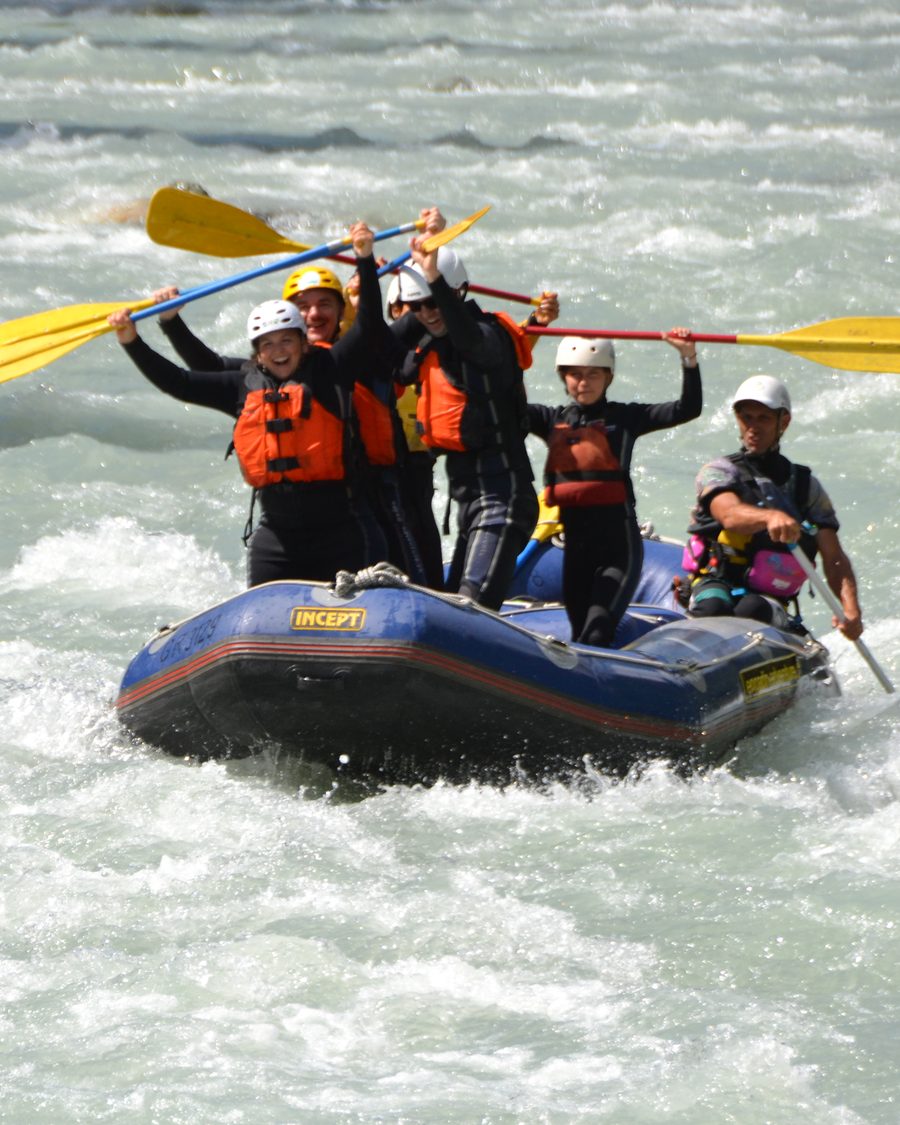 Een groep in een raft op wild water, met de peddels omhoog.