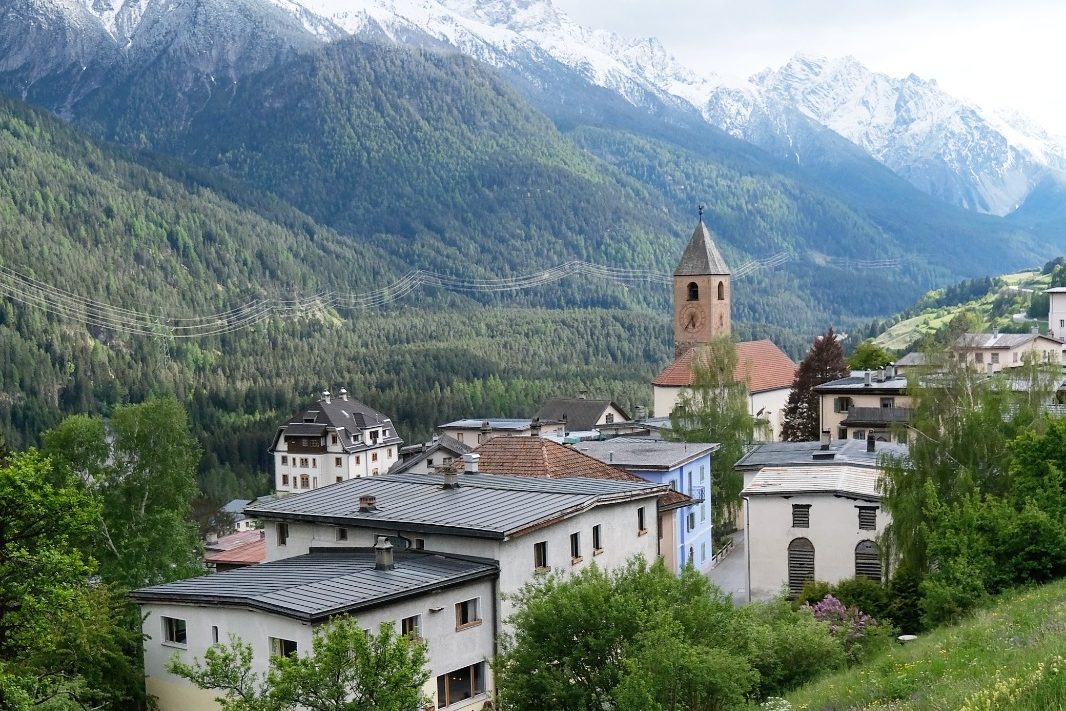 The village with its church tower in the green valley, with snow-capped peaks behind.