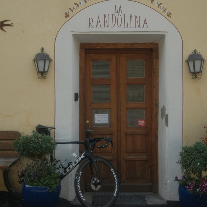 Die Haustür des La Randulina mit dem aufgemalten Namen über dem Bogen und einem Rennrad, das daran lehnt.