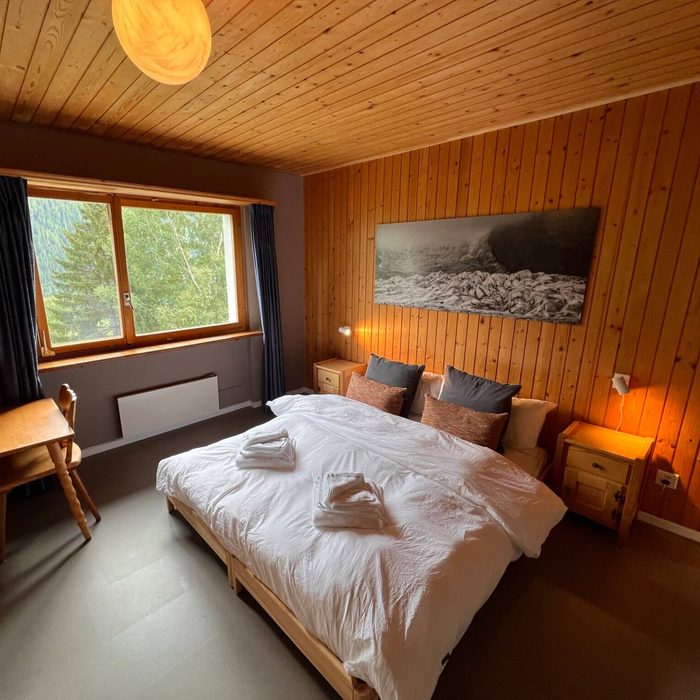 Ein Doppelzimmer mit gemachtem Bett, einer runden Hängelampe und einem Schwarz-Weiss-Foto eines Gletschers über dem Bett.