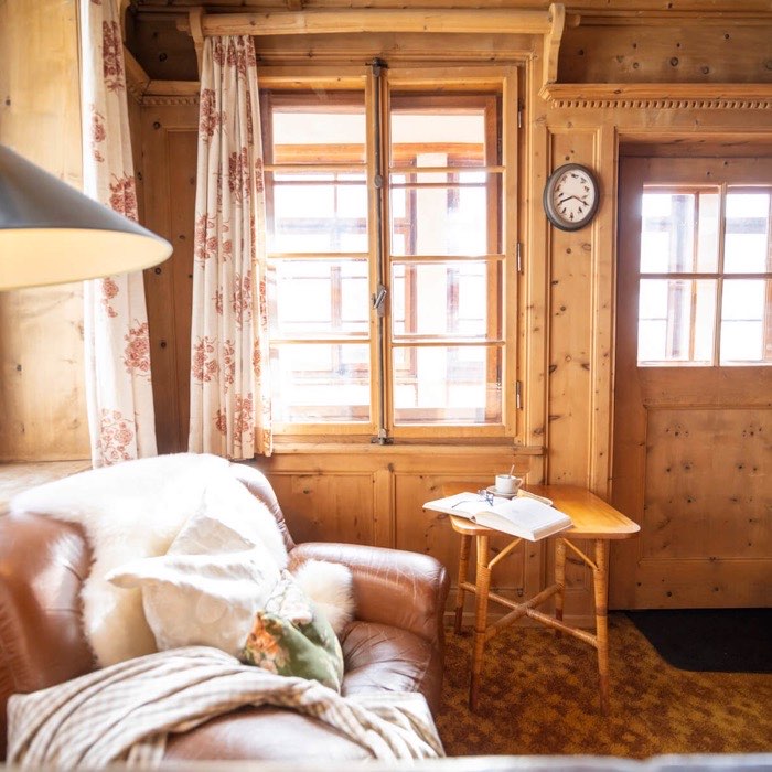 Een leeshoek in de lodge: een leren fauteuil met een schapenvacht, een oude wandklok en een bijzettafel met een boek.
