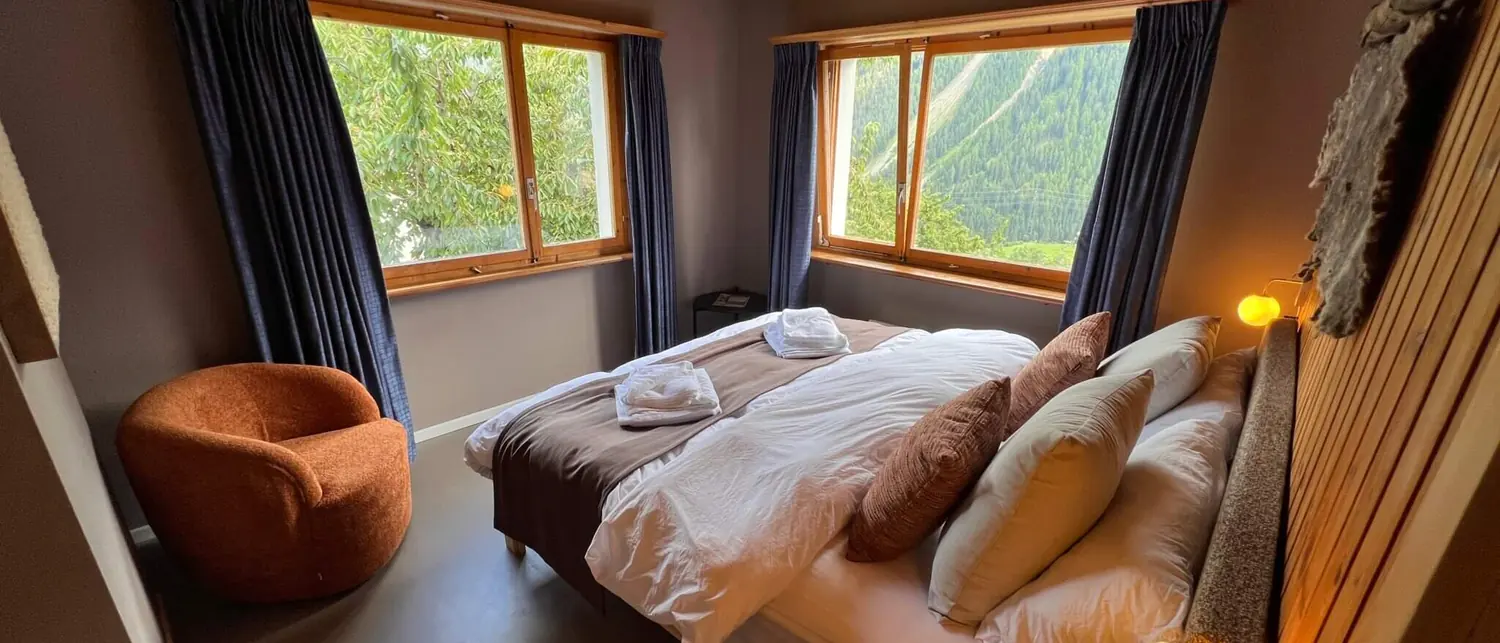 A room with dark linen, a rust-coloured armchair and two windows looking out over the wooded valley.