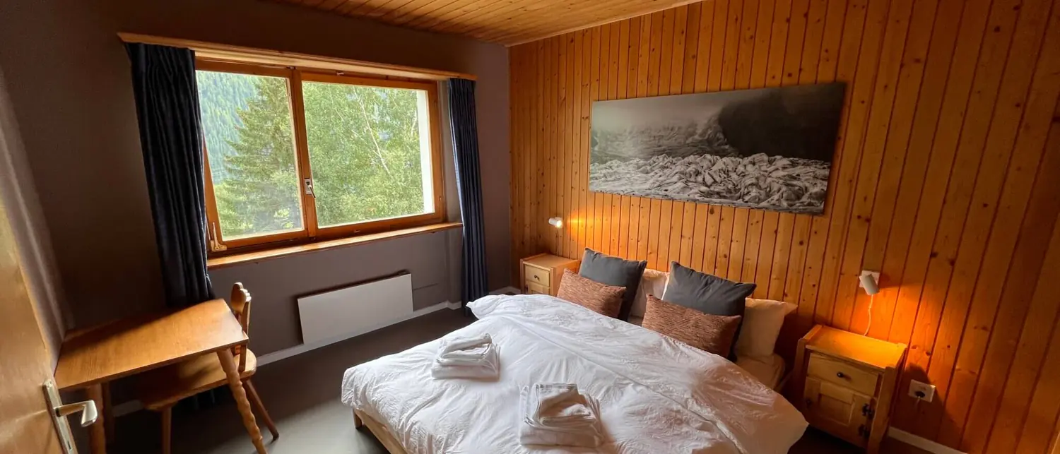 A room with pine panelling, bedside lamps switched on and a black-and-white photo of a glacier above the bed.