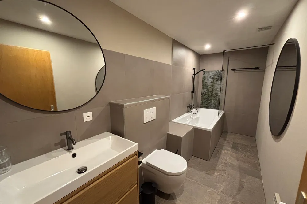 A bathroom with a washbasin, round mirrors, a shower and a bath.