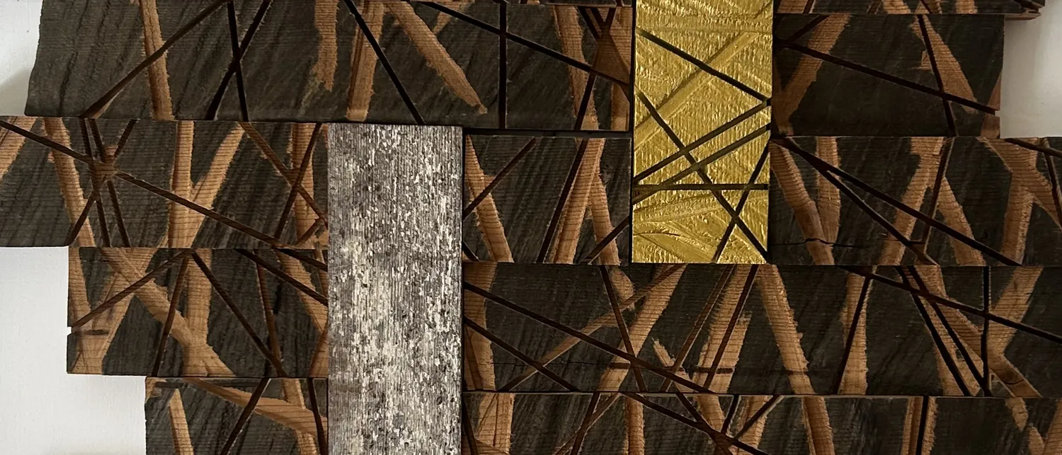 Van dichtbij: verbrand donker hout met ingekraste lijnen, met bladgoud en een strook verweerd staal.