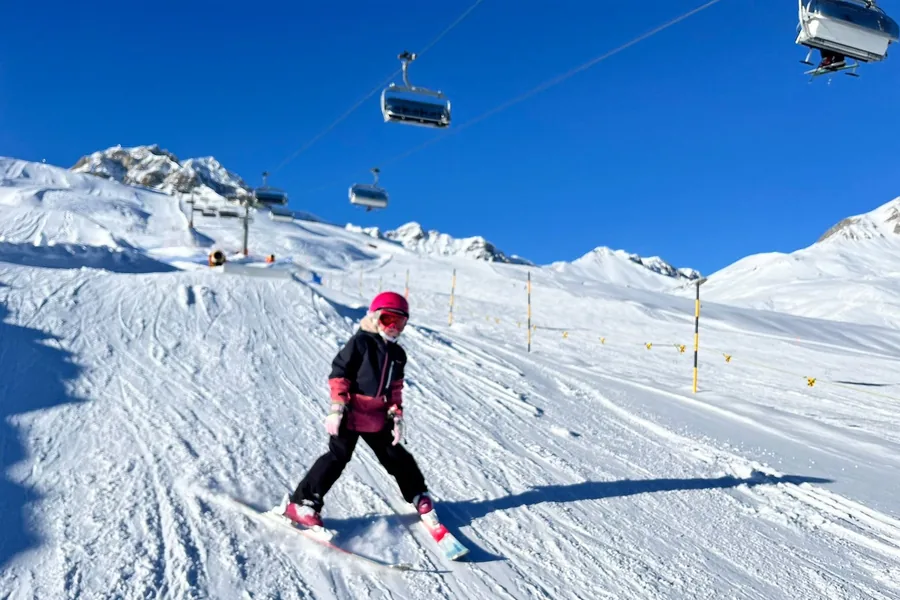 A child skiing down a wide piste beneath a chairlift.