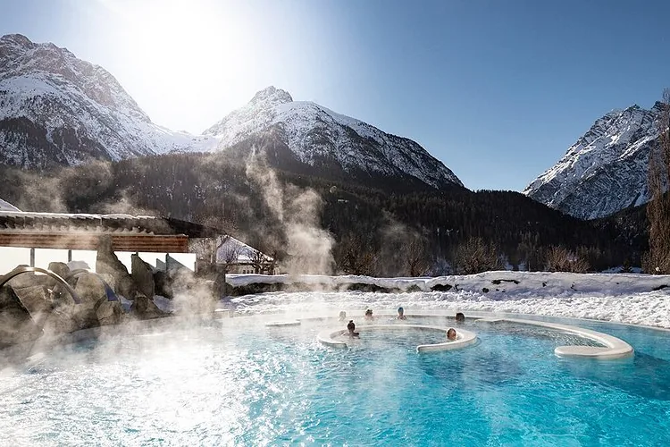 Das dampfende Aussenbecken des Bogn Engiadina in Scuol, dahinter verschneite Berge.