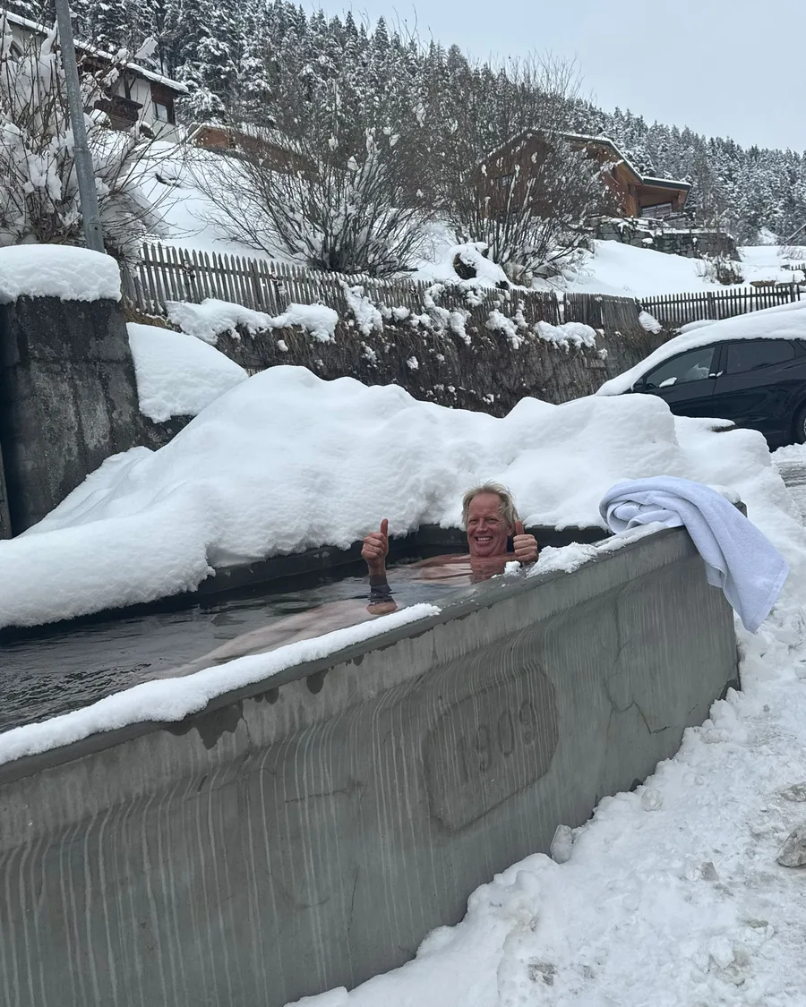 Jemand sitzt bis zu den Schultern im eiskalten Wasser der Quelle, zwischen hohen Schneerändern.