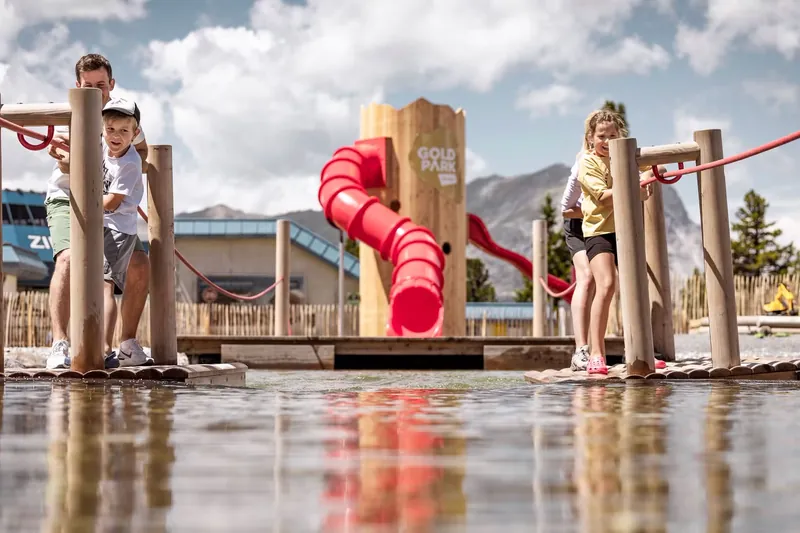 Kinderen spelen op een houten speeltoestel met een rode glijbaan.
