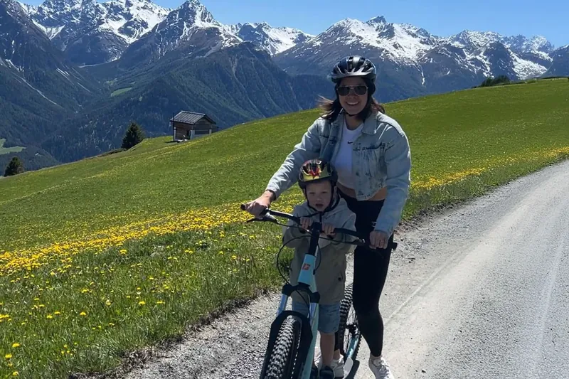 Een moeder en kind op een fiets op een grindweg door een bergweide.