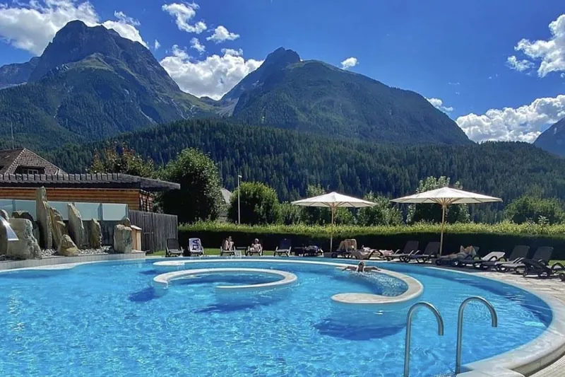 Een buitenbad met ligstoelen en parasols, met de bergen erachter.
