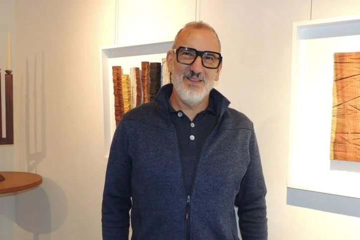 In de expositieruimte, tussen ingelijste wandobjecten van hout.
