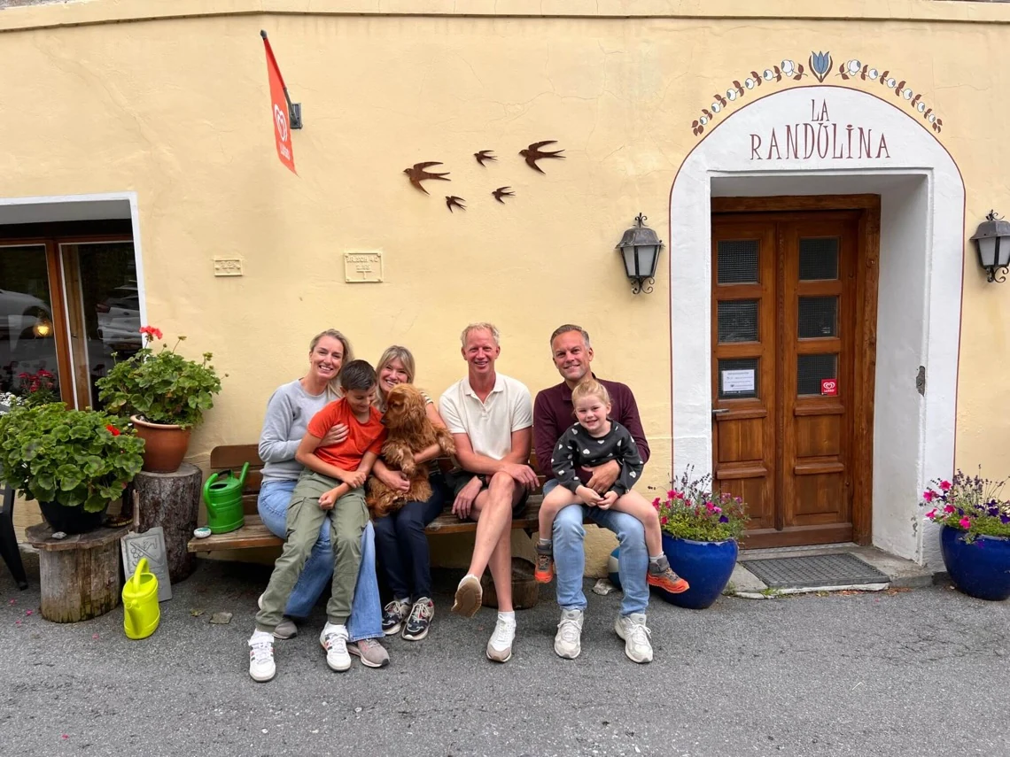 Eine Gruppe von Erwachsenen und Kindern mit einem Hund auf der Holzbank vor dem Eingang von La Randulina.